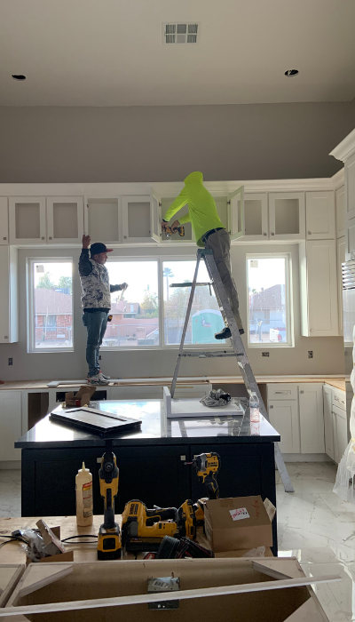 Técnicos instalando gabinetes superiores en cocina blanca con isla central y piso de mármol – servicio de carpintería fina y remodelación de interiores residenciales